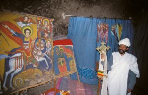 Priester mit Kreuz neben religiöser Malerei